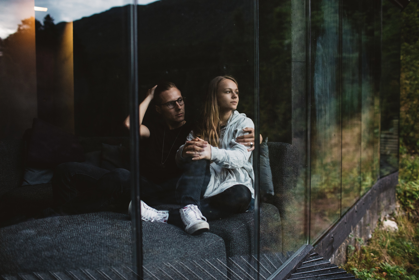 A couple sitting together, looking out over a mountain landscape through a glass wall